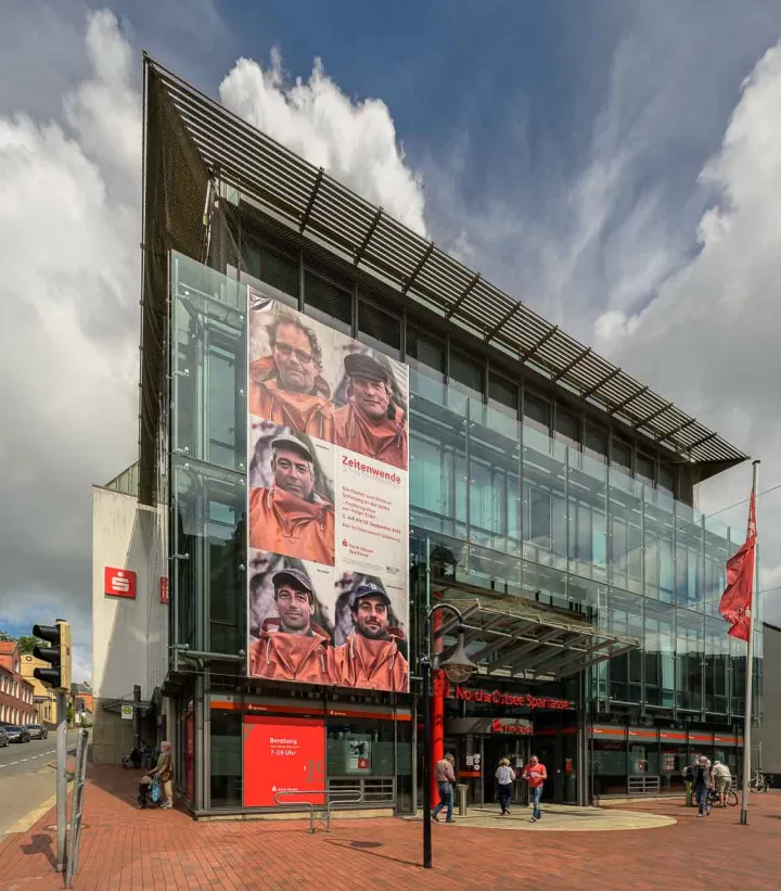 Außenbanner Ausstellung "Zeitenwende" (farbige Version" Mit den monumentalen Porträts der fünf Schleifischer vom Holm wirbt ein Außenbanner an der Nord-Ostsee Sparkasse in Schleswig für einen Besuch der Ausstellung "Zeitenwende" (farbige Version).