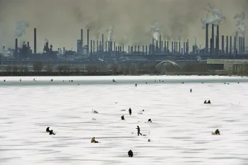 An Winterwochenenden bohren Männer Löcher ins dicke Eis des Ural und versuchen ihr Glück beim Angeln. Da sie wissen, wie stark das Lenin-Stahlwerk im Hintergrund den Fluss verschmutzt, verzehren sie ihren Fang in der Regel nicht selbst, sondern verkaufen ihn auf dem Markt. Magnitogorsk, Russland 1993 © Gerd Ludwig